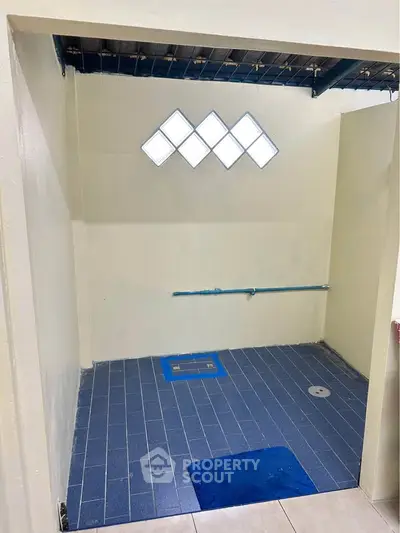 Spacious bathroom with modern blue tile flooring and unique diamond-shaped window design.