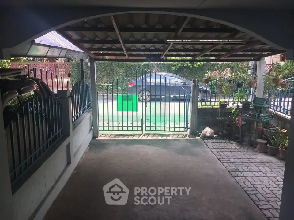 Spacious covered parking area with gated entrance and garden view, ideal for secure vehicle storage.