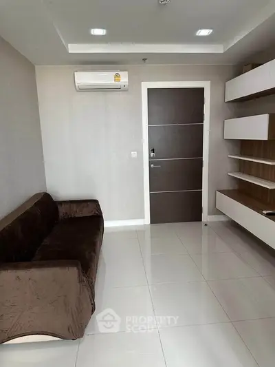 Modern living room with sleek brown sofa and wall-mounted shelves, featuring a minimalist design and air conditioning.