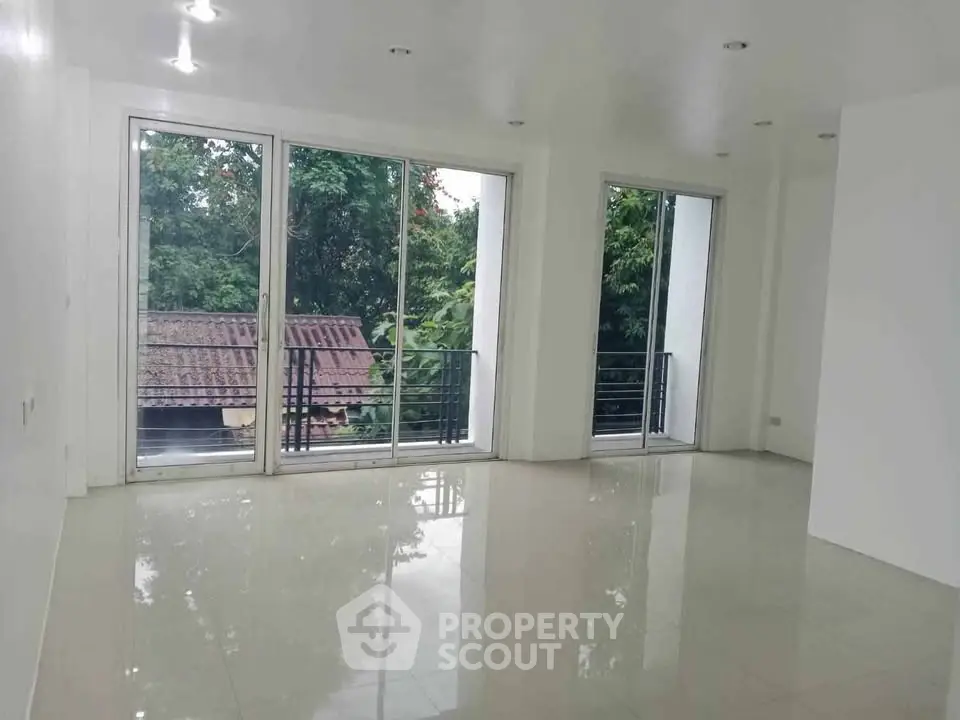 Spacious living room with large windows and serene greenery view, perfect for natural light lovers.
