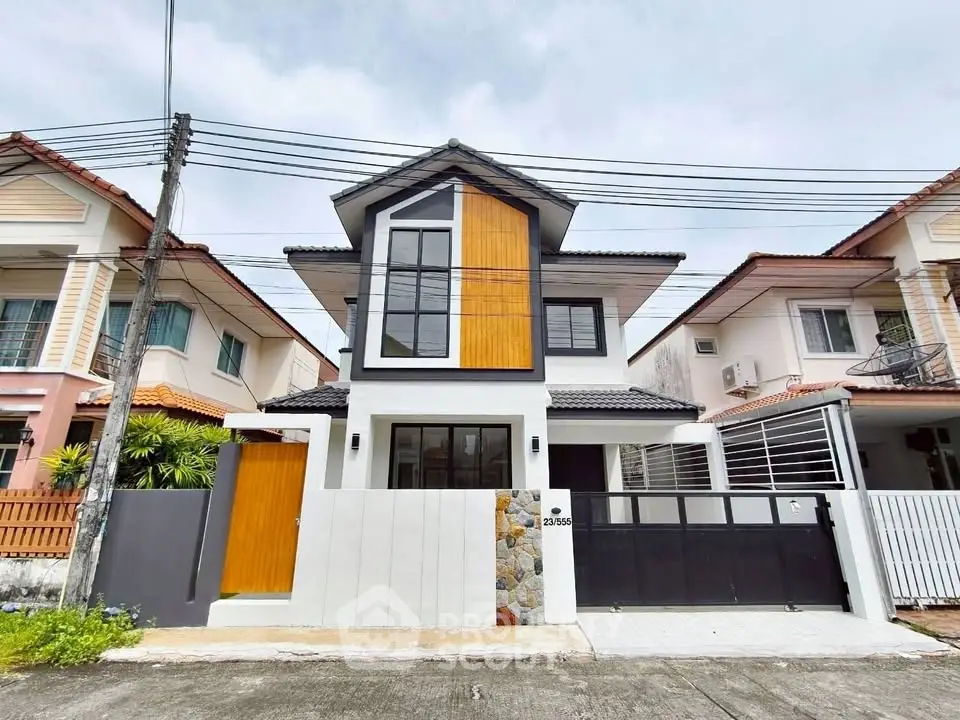 Modern two-story house with unique facade and gated entrance in suburban neighborhood.