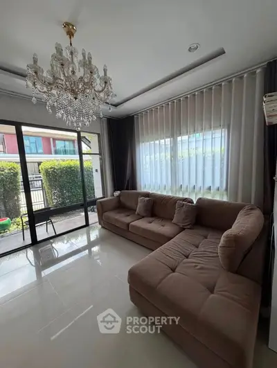 Elegant living room with chandelier and large windows overlooking garden, featuring a plush sectional sofa.