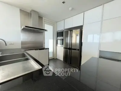 Modern kitchen with sleek appliances and black countertops, featuring a stainless steel fridge and oven.