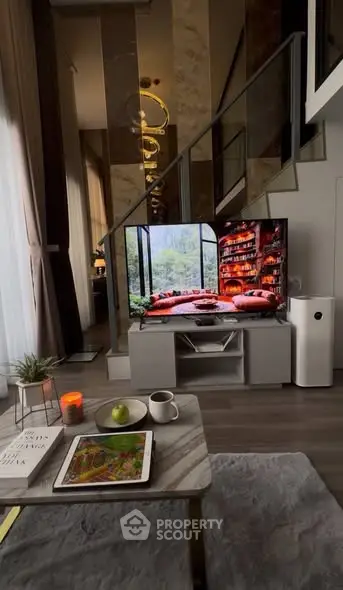 Modern living room with stylish decor and large TV under elegant staircase.