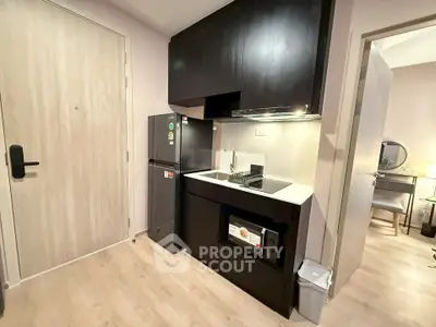Modern compact kitchen with sleek black cabinets and integrated appliances in a stylish apartment.