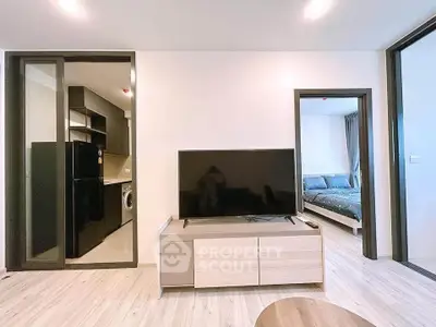 Modern living room with sleek TV setup and view into kitchen and bedroom, showcasing open layout.