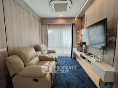 Modern living room with plush recliner sofas and large wall-mounted TV, featuring elegant wood paneling and natural light.