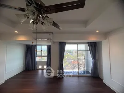 Spacious living room with ceiling fan and large windows offering city views.