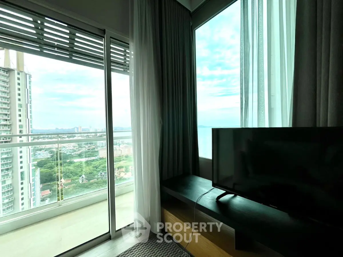 Modern living room with large windows offering stunning city and ocean views, featuring a sleek TV setup.