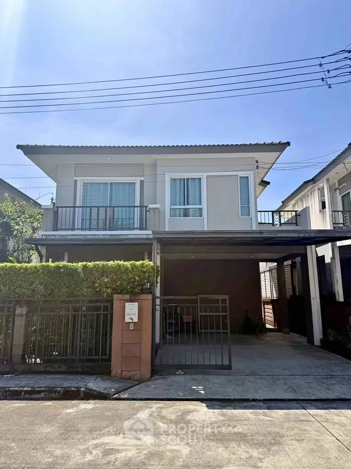 Modern two-story house with balcony and gated driveway in sunny neighborhood.