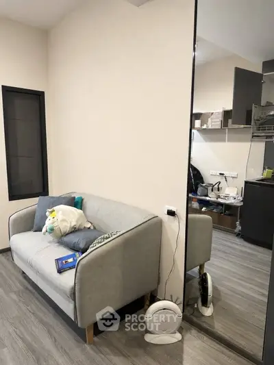 Modern living room with cozy gray sofa and sleek wooden flooring, adjacent to a compact kitchen area.