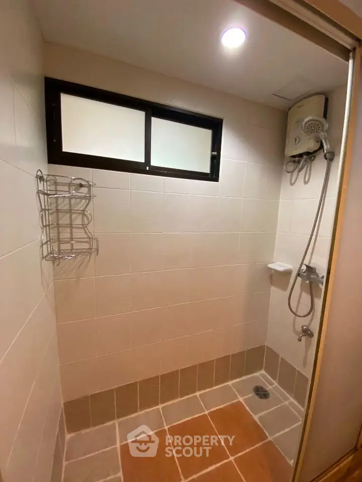 Compact bathroom with shower and tiled walls, featuring a window for natural light.