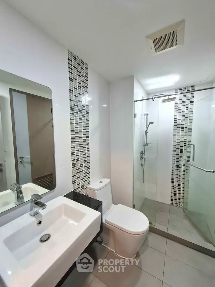 Modern bathroom with sleek design, featuring a glass shower enclosure and stylish tile accents.