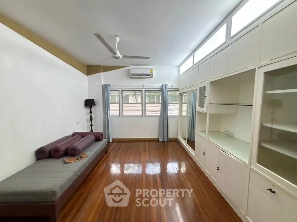 Spacious living room with wooden flooring and built-in storage, featuring large windows for natural light.
