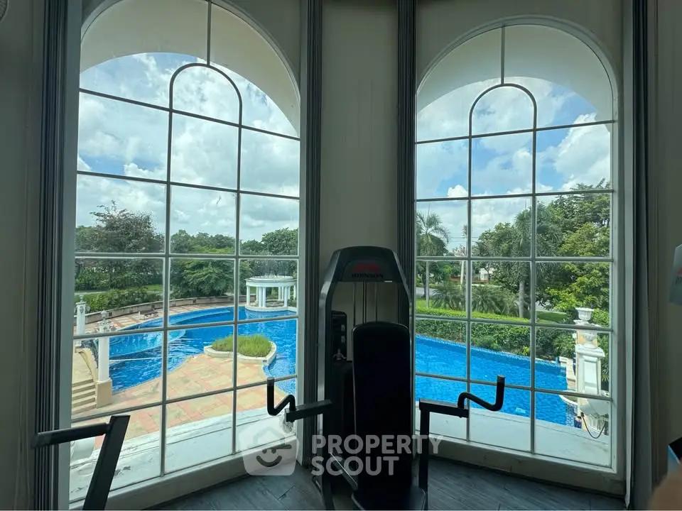 Luxurious gym with stunning pool view through large arched windows, perfect for fitness enthusiasts.