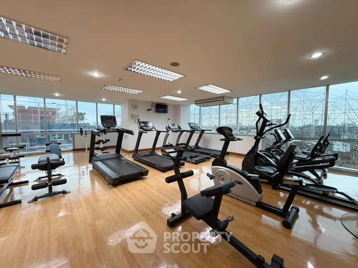 Spacious gym with modern equipment and large windows offering city views.