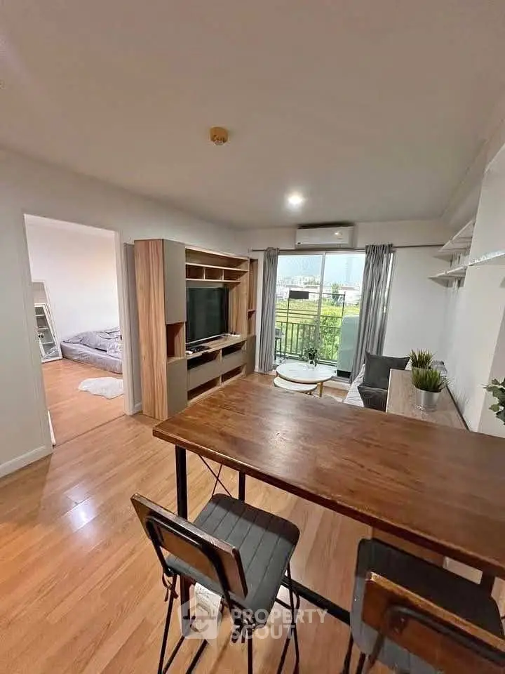 Modern open-plan living room with wooden flooring and stylish furniture, featuring a view of the bedroom and balcony.