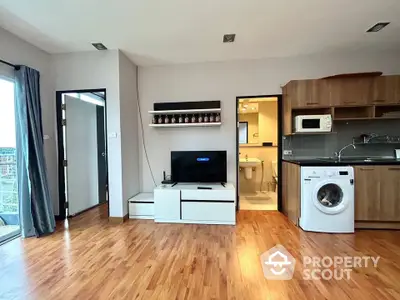 Modern living room with wooden flooring, TV, and kitchen appliances in open layout apartment.