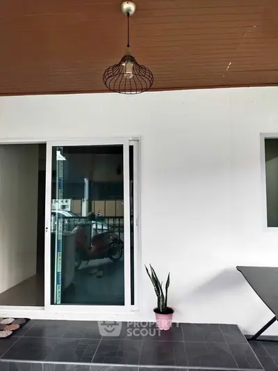 Modern patio with sliding glass door and potted plant, featuring stylish ceiling light.