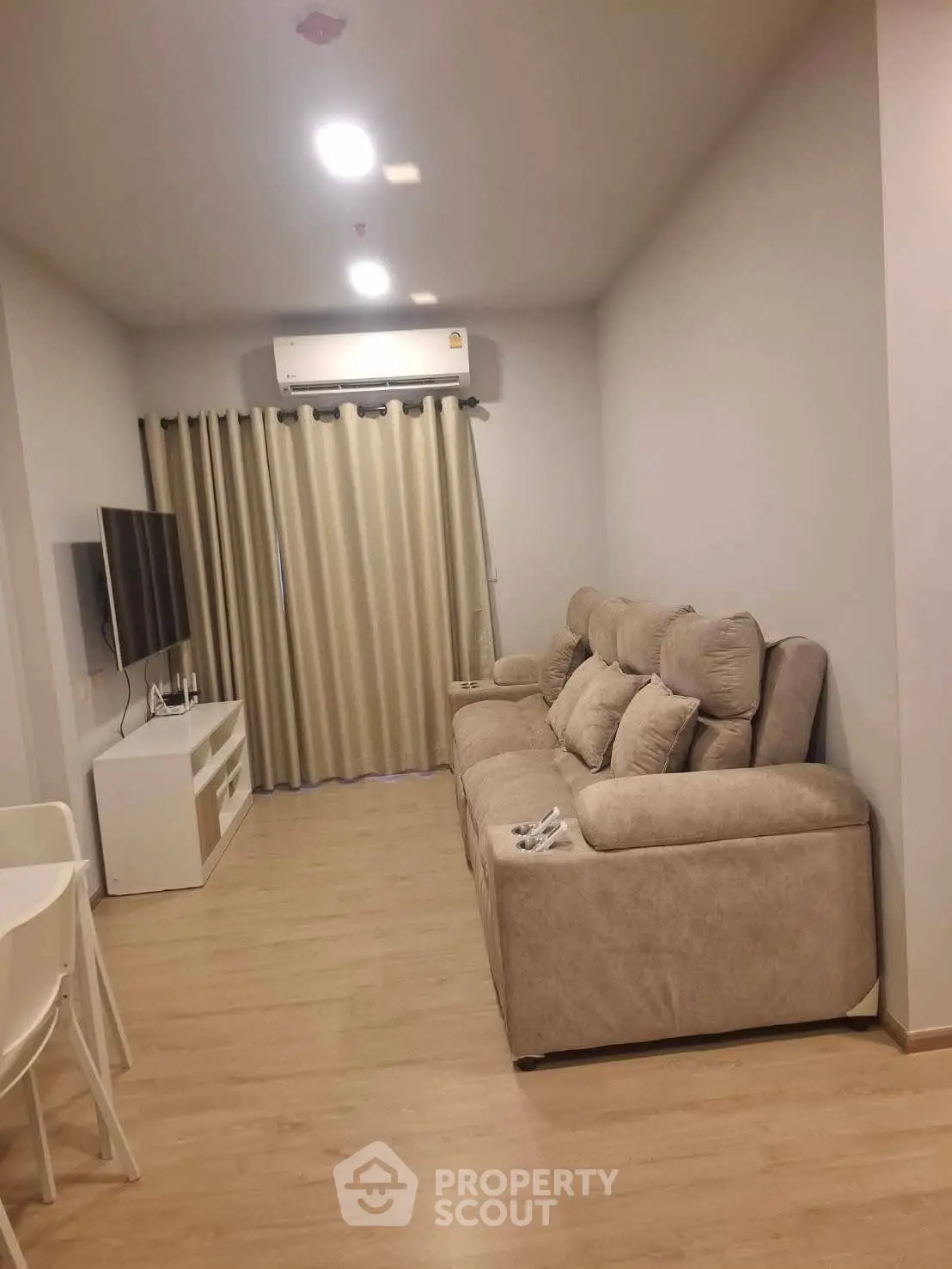 Modern living room with cozy sofa and flat-screen TV, featuring elegant curtains and wooden flooring.