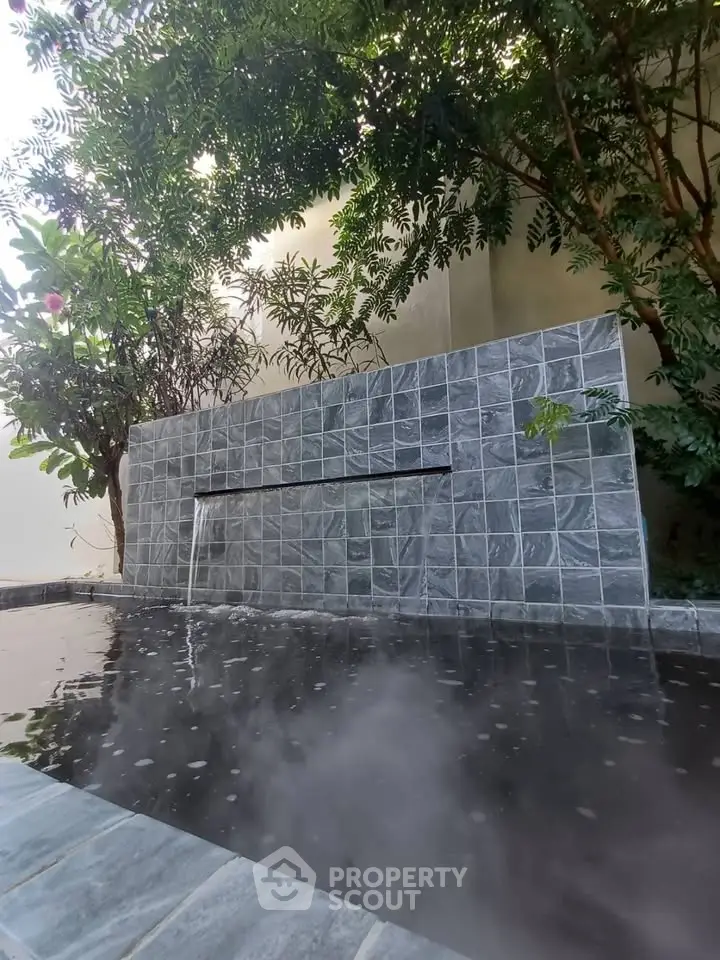 Luxurious outdoor pool with elegant stone waterfall feature and lush greenery