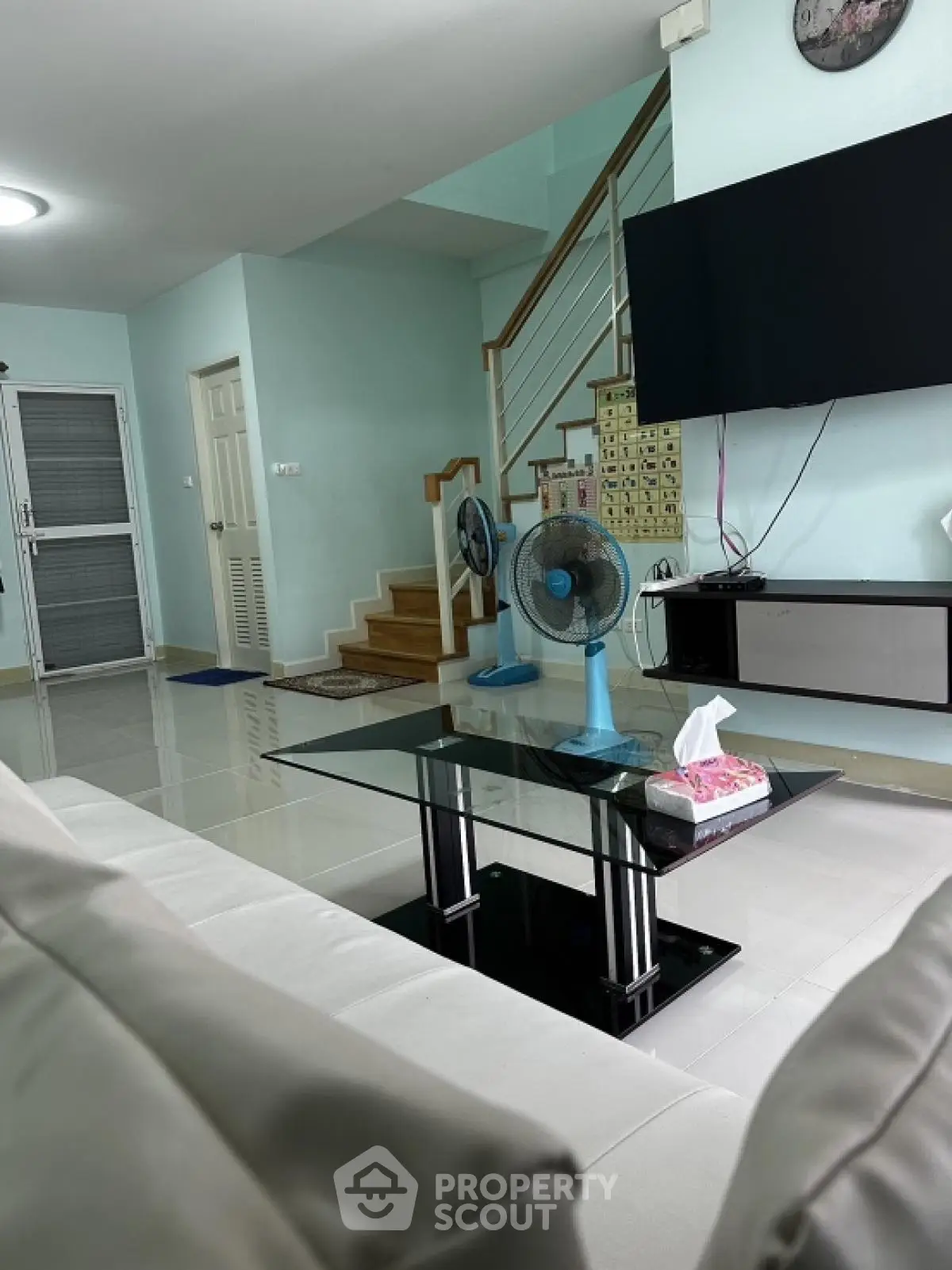 Modern living room with sleek furniture and staircase, featuring a large TV and stylish glass coffee table.
