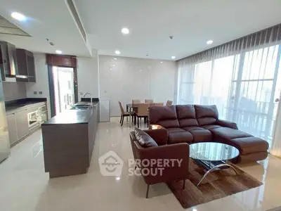 Spacious modern living room with open kitchen and dining area, featuring sleek furniture and abundant natural light.
