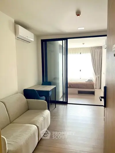 Modern apartment interior with cozy living room and bedroom separated by glass doors.