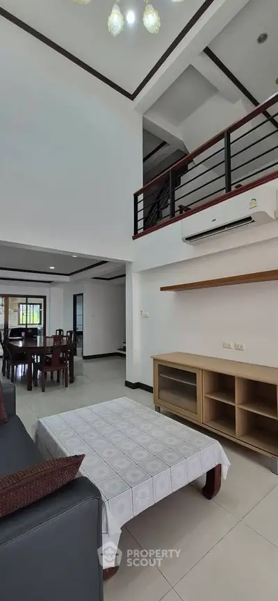 Spacious modern living room with high ceiling and mezzanine, featuring elegant furniture and open layout.