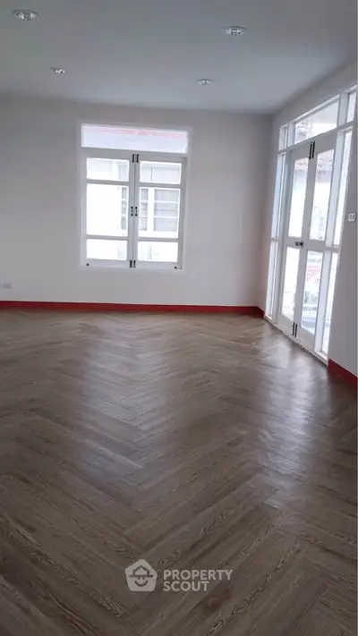 Spacious empty room with large windows and wooden flooring, perfect for customization.