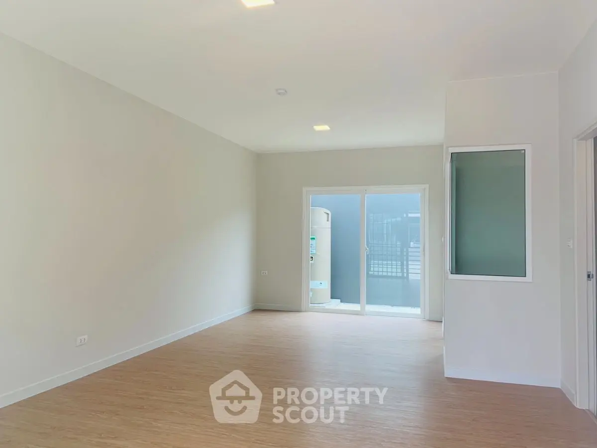 Spacious empty room with wooden flooring and balcony access in modern apartment.