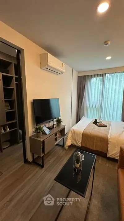 Modern bedroom with cozy decor and natural light, featuring a TV and air conditioning.