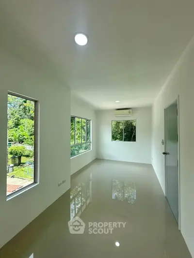 Spacious empty room with large windows and glossy tiled floor, offering serene garden views.