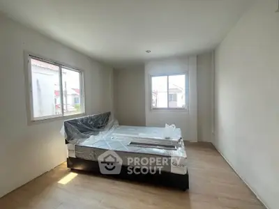 Spacious bedroom with large windows and natural light, featuring a new bed with protective covering.