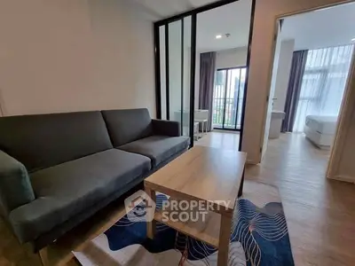 Modern living room with sleek sofa and wooden coffee table, leading to a bright bedroom with balcony view.