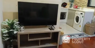 Modern living room with TV stand and adjacent kitchen featuring washing machine and microwave.