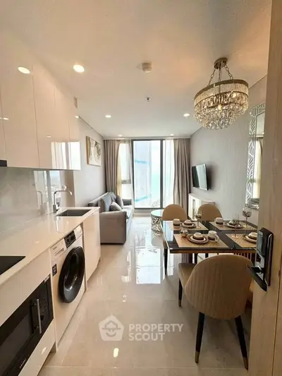 Modern open-plan living room and kitchen with elegant dining area and chandelier.