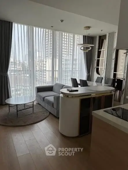 Modern living room with large windows and city view, featuring sleek furniture and open layout.