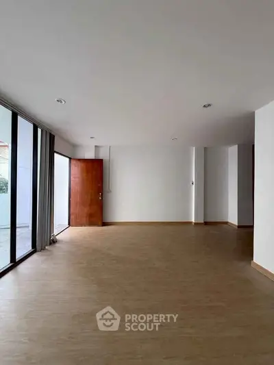 Spacious empty living room with wooden floor and large windows.