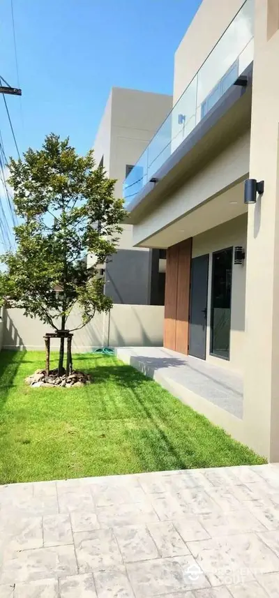 Modern minimalist home exterior with lush green lawn and sleek balcony design.