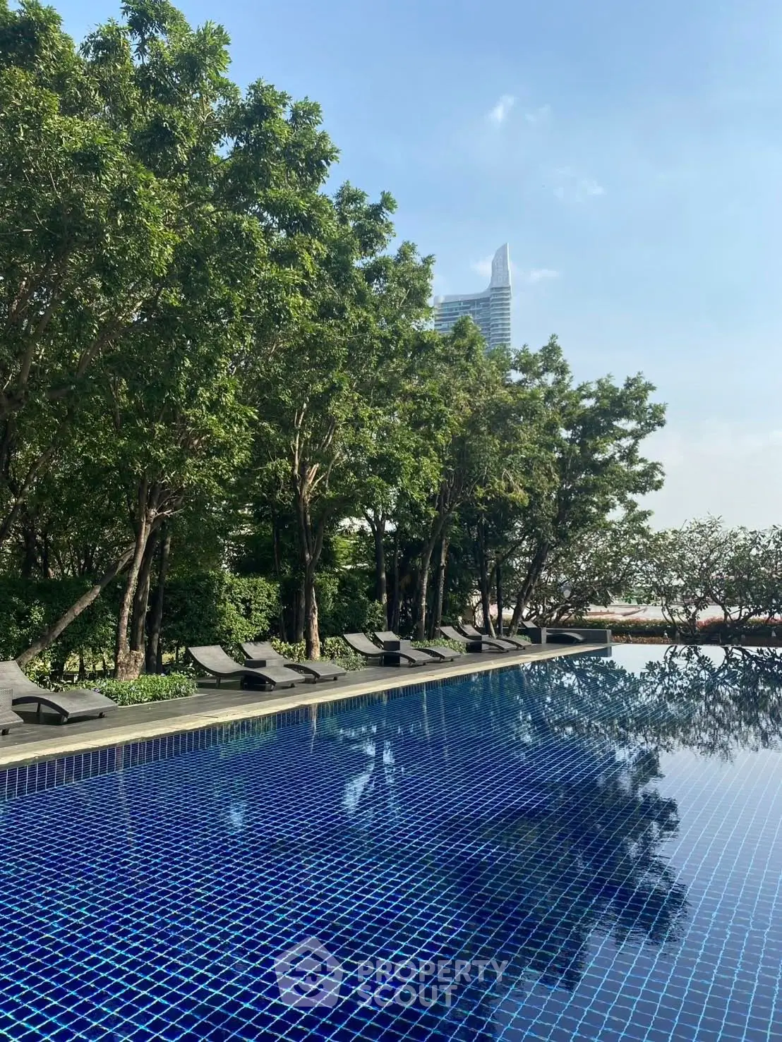 Luxurious outdoor pool area with modern lounge chairs and lush greenery, perfect for relaxation and leisure.