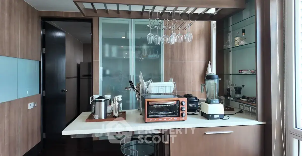 Modern kitchen with wooden cabinets, glass rack, and appliances including blender and oven.
