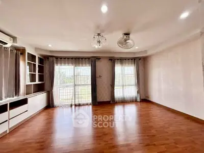 Spacious living room with wooden flooring and large windows offering natural light.