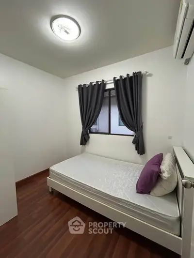 Cozy bedroom with wooden flooring and modern lighting, featuring a comfortable bed and air conditioning.