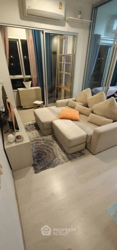 Modern living room with cozy beige sofa, stylish decor, and large windows offering natural light.