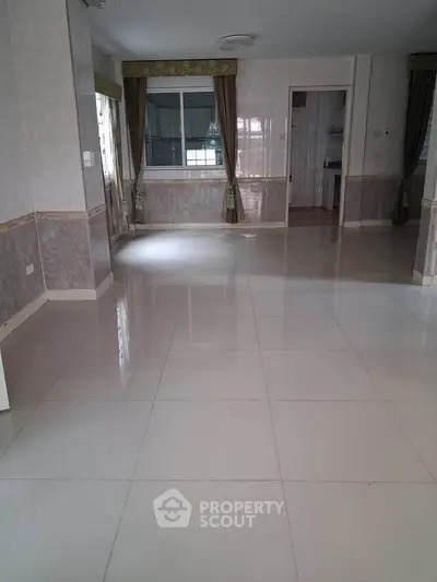 Spacious empty living room with large windows and tiled flooring, perfect for customization.