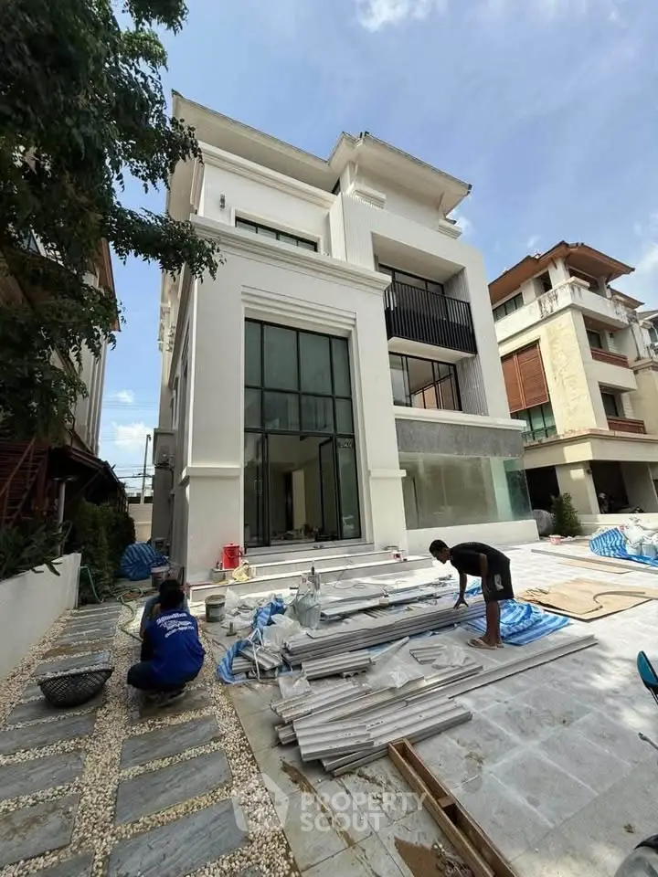 Modern three-story house under construction with spacious windows and outdoor area.