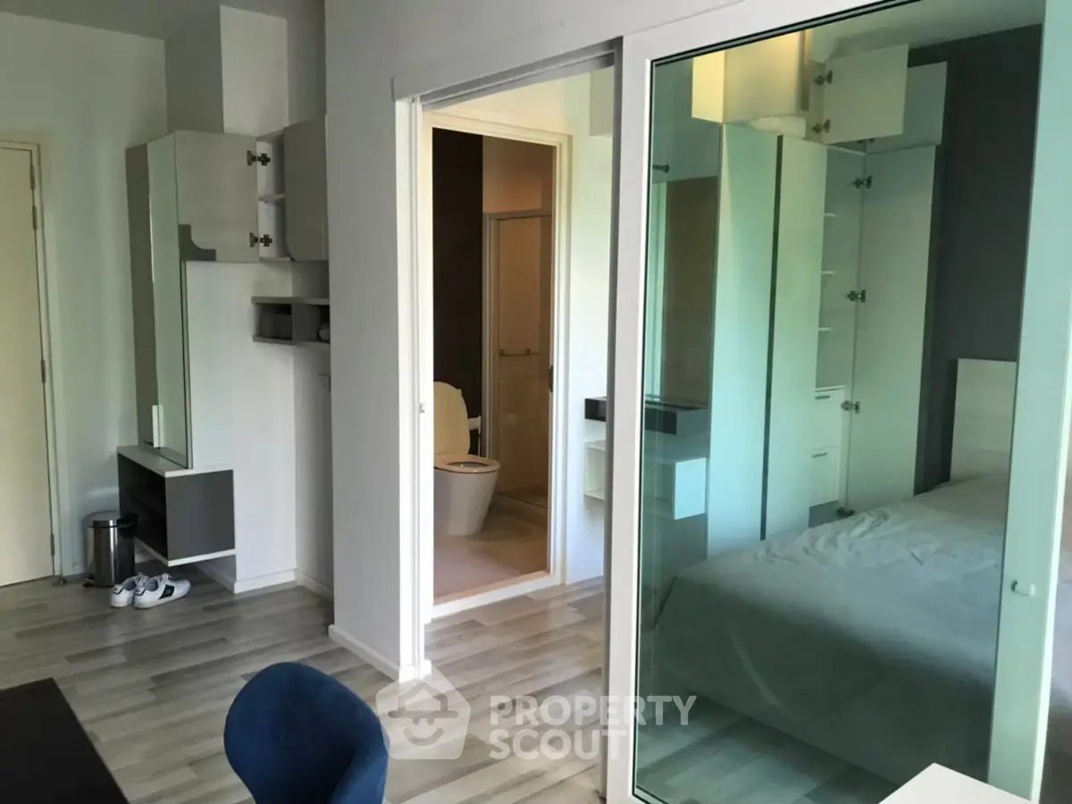 Modern apartment interior with glass partition, showcasing bedroom and bathroom.