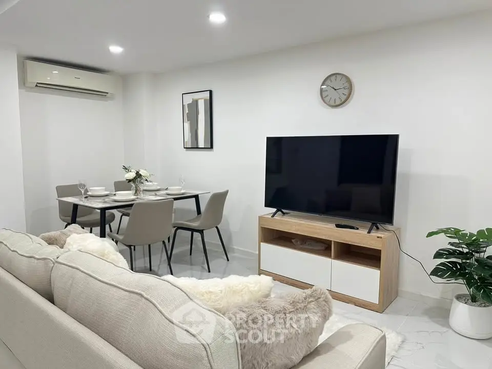 Modern living room with dining area, featuring sleek furniture and a wall-mounted TV.