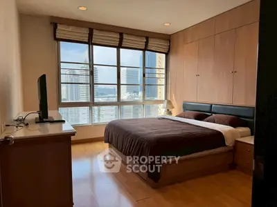 Spacious bedroom with city view and modern furnishings in high-rise apartment.